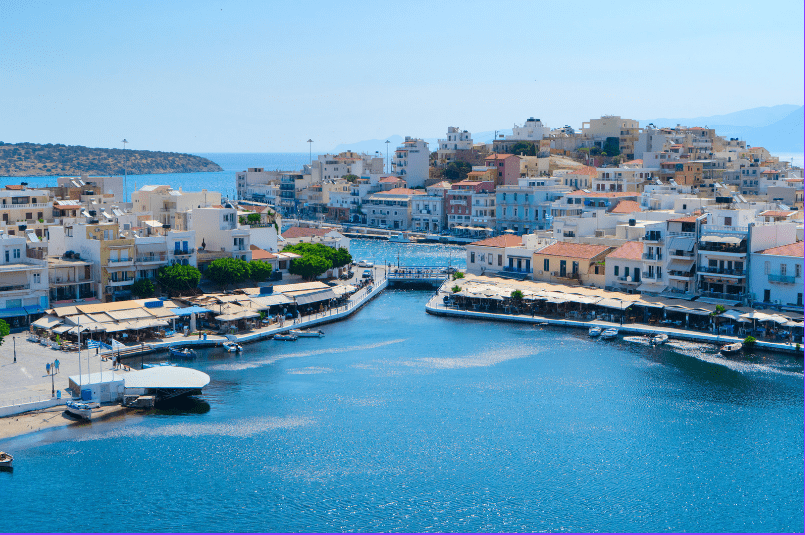 Coastal view of a harbor with boats and buildings lining the waterfront in a Mediterranean setting.