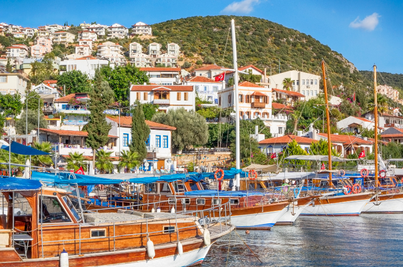 Wooden boats docked in a harbor with residential buildings on a hillside in the background under a clear blue sky. hidden gems in turkey